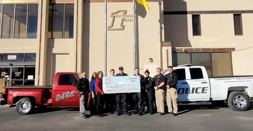 Officers with bank employees in front of a red and a white truck