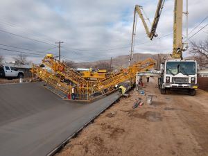 Workers and large equipment working on cement in a ditch